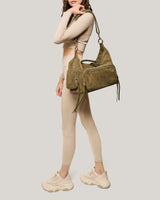 A woman wearing a white top and pants showing off this suede duffle bag that's perfect for a weekend getaway. 