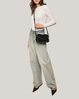 A woman wearing a white shirt and jeans, showing off this sleek suede mini bag 