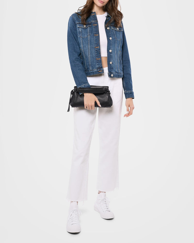 A woman wearing a denim jacket and white pants showcasing the leather crossbody bag as a clutch purse. 